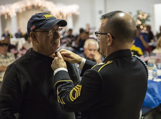 SFC Ralph Walton, of the U.S.A. Vietnam War 50th Commemoration, pins a Vietnam veteran.