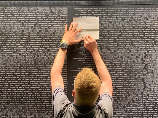A man reaches up on The Wall That Heals to rub a name on a paper