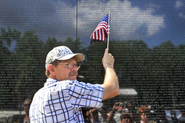 A man uses an American flag to point to a name on the Vietnam Veterans Memorial after a ceremony com