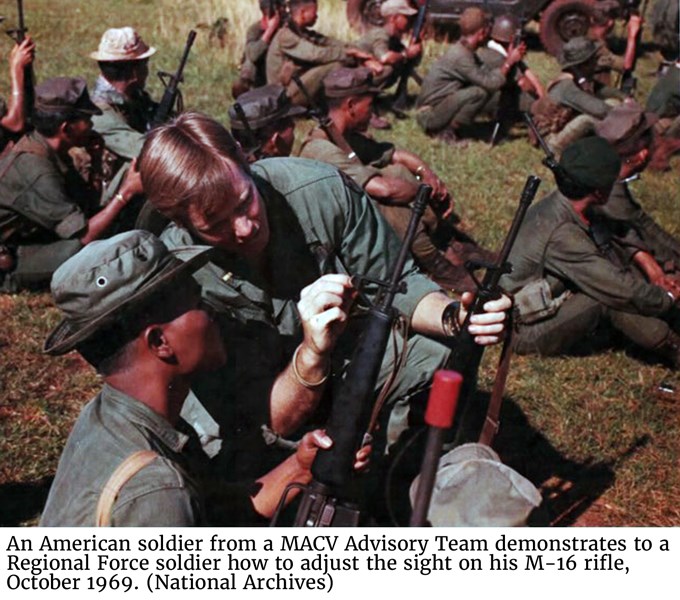 An American soldier from a MACV Advisory Team demonstrates to a Regional Force soldier how to adjust the sight on his M-16 rifle, October 1969. (National Archives)