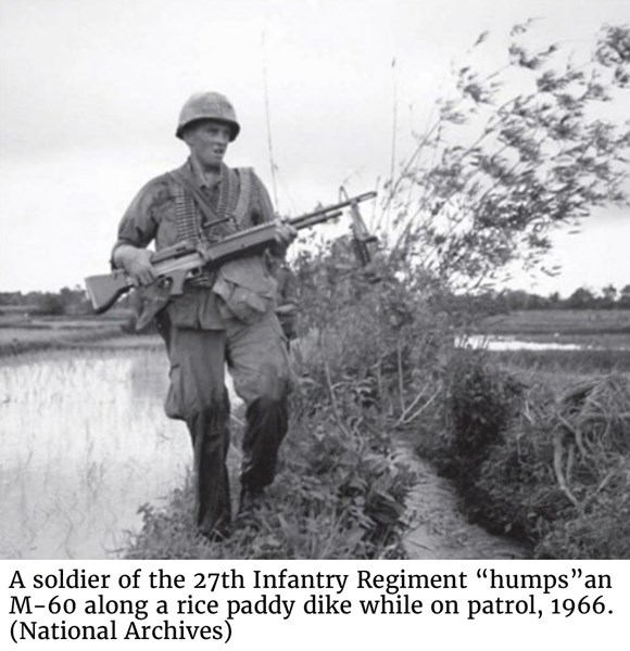 A soldier of the 27th Infantry Regiment “humps” an M-60 along a rice paddy dike while on patrol, 1966. (National Archives) 