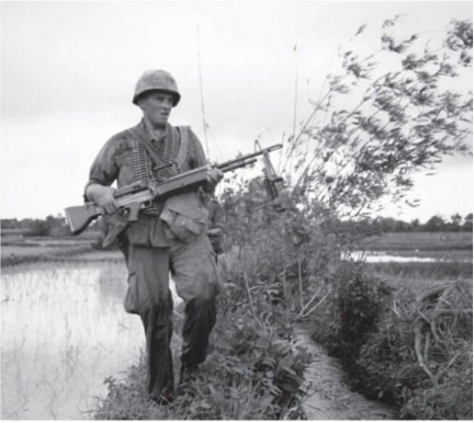 A soldier of the 27th Infantry Regiment “humps” an M-60 along a rice paddy dike while on patrol, 1966. (National Archives) 